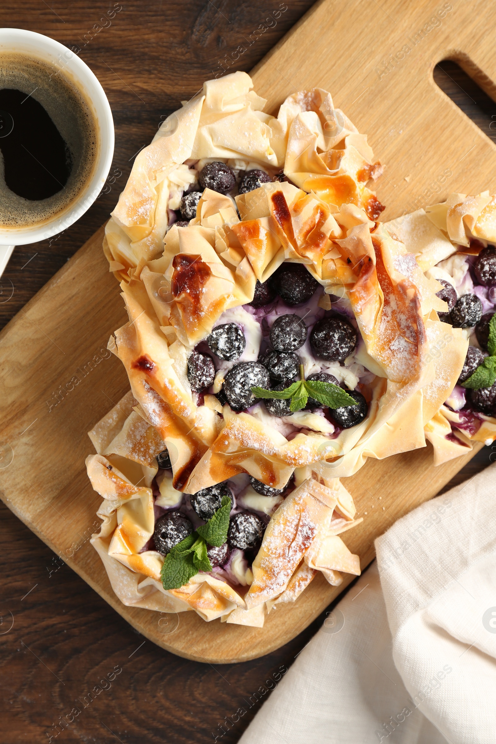 Photo of Tasty puff pastries with blueberries, powdered sugar, mint and coffee on wooden table, top view