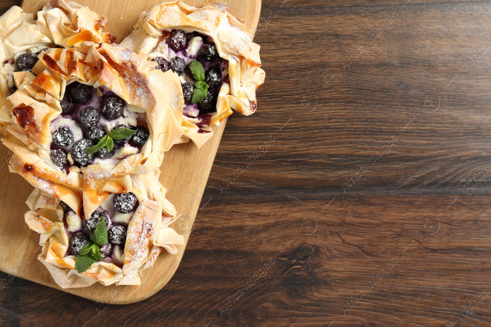 Photo of Tasty puff pastries with blueberries, powdered sugar and mint on wooden table, top view. Space for text