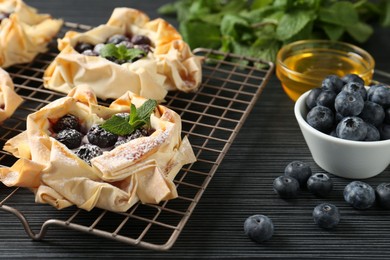 Photo of Tasty puff pastries with blueberries, powdered sugar, mint and honey on dark table, closeup