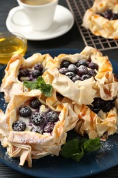 Photo of Tasty puff pastries with blueberries, powdered sugar, mint, coffee and honey on table, closeup