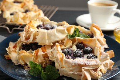 Tasty puff pastries with blueberries, powdered sugar, mint and coffee on dark table, closeup