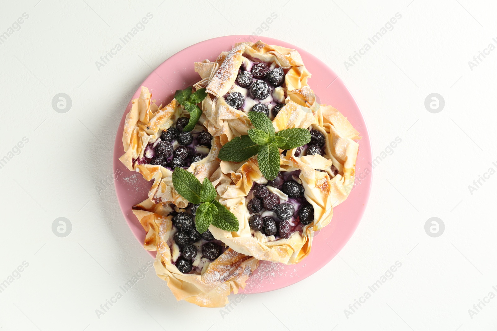 Photo of Tasty puff pastries with blueberries, powdered sugar and mint on white table, top view