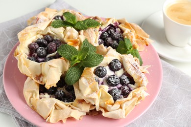 Photo of Tasty puff pastries with blueberries, powdered sugar, mint and coffee on table, closeup