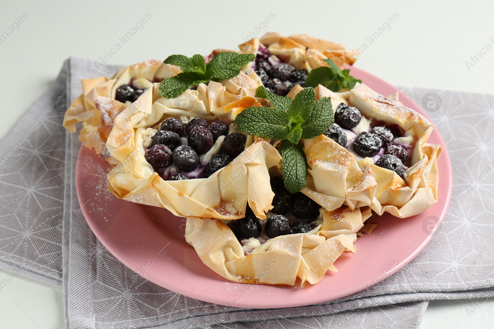 Photo of Tasty puff pastries with blueberries, powdered sugar and mint on white table, closeup