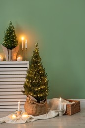 Photo of Small spruce trees with Christmas lights and other decor near green wall indoors