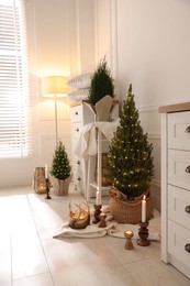 Photo of Small spruce trees with Christmas lights and other decor indoors