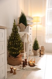 Photo of Small spruce trees with Christmas lights and other decor indoors