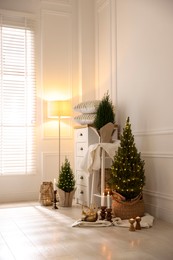 Photo of Small spruce trees with Christmas lights and other decor indoors