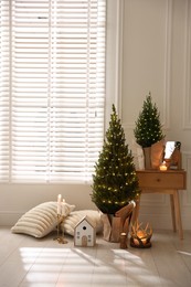 Photo of Small spruce trees with Christmas lights and other decor indoors