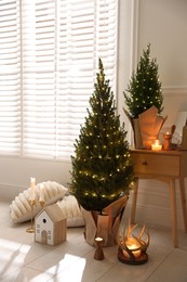 Photo of Small spruce trees with Christmas lights and other decor indoors