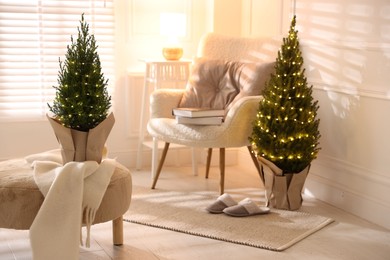 Photo of Small spruce trees decorated with Christmas lights indoors