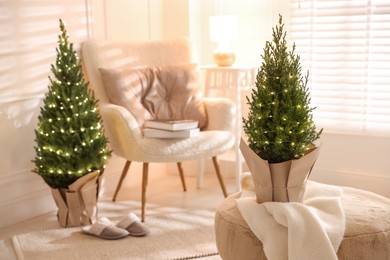 Photo of Small spruce trees decorated with Christmas lights indoors