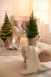 Photo of Small spruce trees decorated with Christmas lights indoors