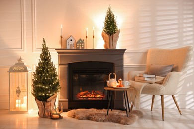 Photo of Small spruce trees decorated with Christmas lights near fireplace indoors