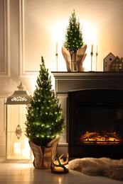 Photo of Small spruce trees decorated with Christmas lights near fireplace indoors