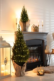 Photo of Small spruce trees decorated with Christmas lights near fireplace indoors