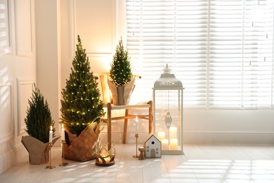 Photo of Small spruce trees with Christmas lights and other decor indoors