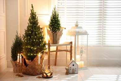 Photo of Small spruce trees with Christmas lights and other decor indoors