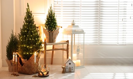 Photo of Small spruce trees with Christmas lights and other decor indoors. Space for text