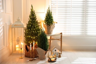 Photo of Small spruce trees with Christmas lights and other decor indoors