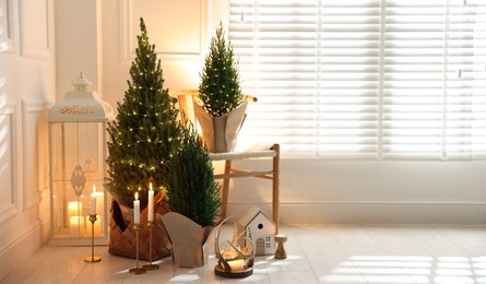 Photo of Small spruce trees with Christmas lights and other decor indoors. Space for text