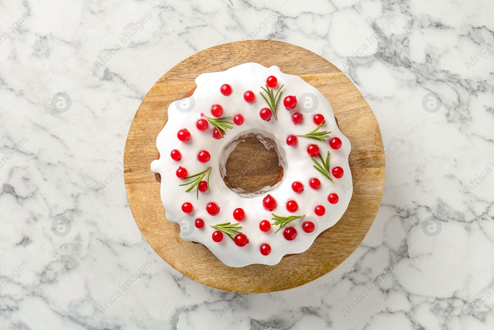 Photo of Traditional Christmas cake decorated with red currants and rosemary on white marble table, top view