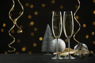 Photo of Delicious champagne in glasses and Christmas decor on black table against blurred lights, space for text