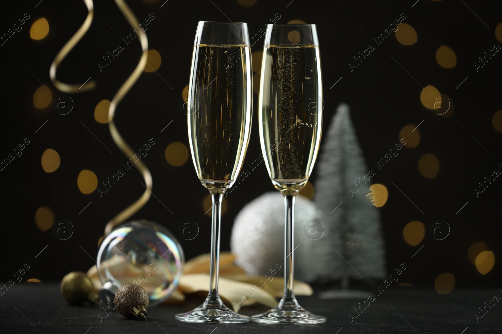 Photo of Delicious champagne in glasses and Christmas decor on black table against blurred lights