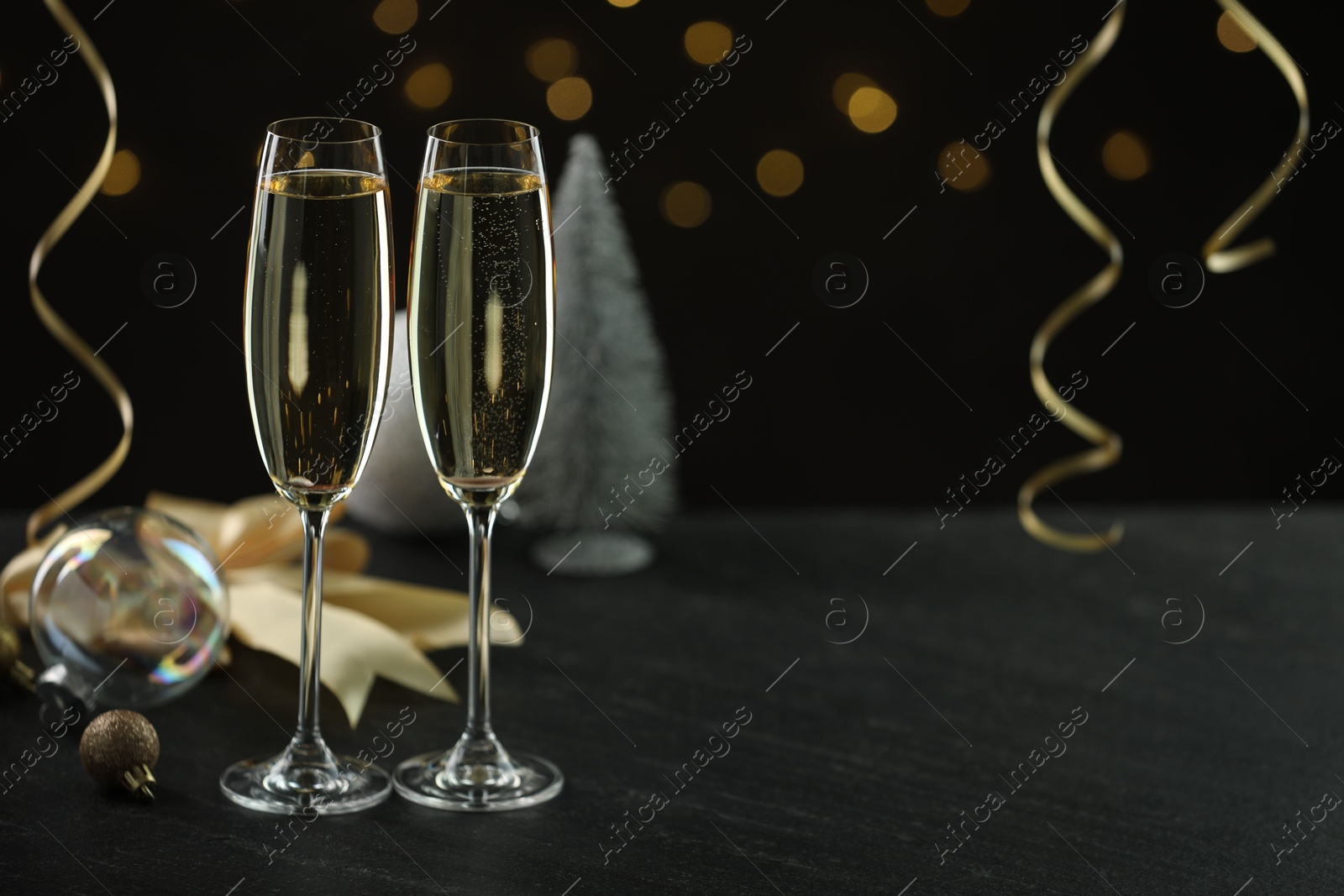 Photo of Delicious champagne in glasses and Christmas decor on black table against blurred lights, space for text