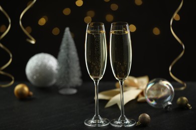 Photo of Delicious champagne in glasses and Christmas decor on black table against blurred lights