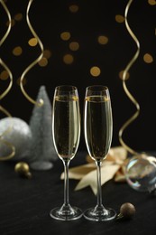 Photo of Delicious champagne in glasses and Christmas decor on black table against blurred lights