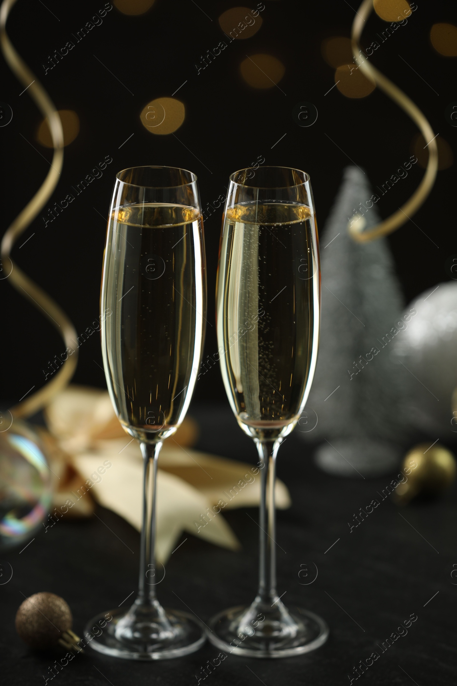 Photo of Delicious champagne in glasses and Christmas decor on black table against blurred lights