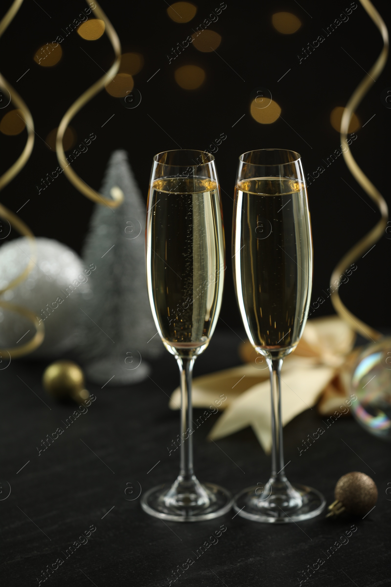 Photo of Delicious champagne in glasses and Christmas decor on black table against blurred lights