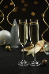 Photo of Delicious champagne in glasses and Christmas decor on black table against blurred lights