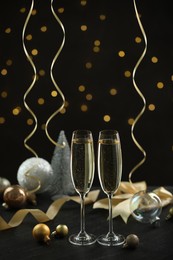 Photo of Delicious champagne in glasses and Christmas decor on black table against blurred lights