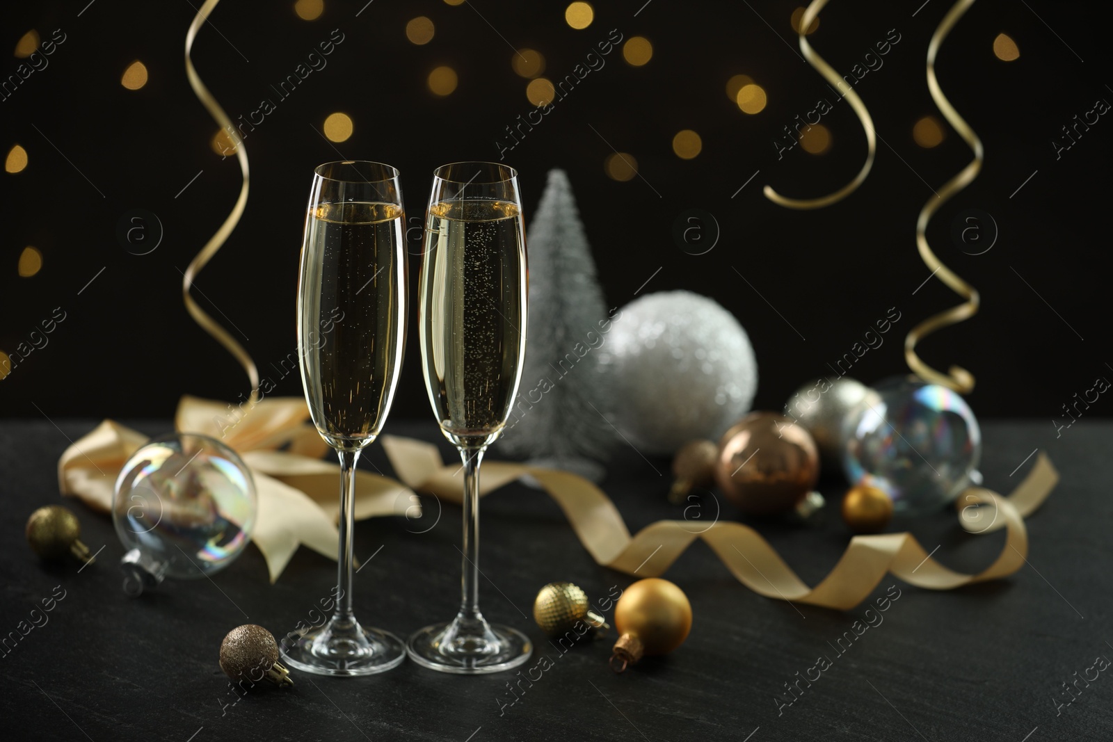 Photo of Delicious champagne in glasses and Christmas decor on black table against blurred lights