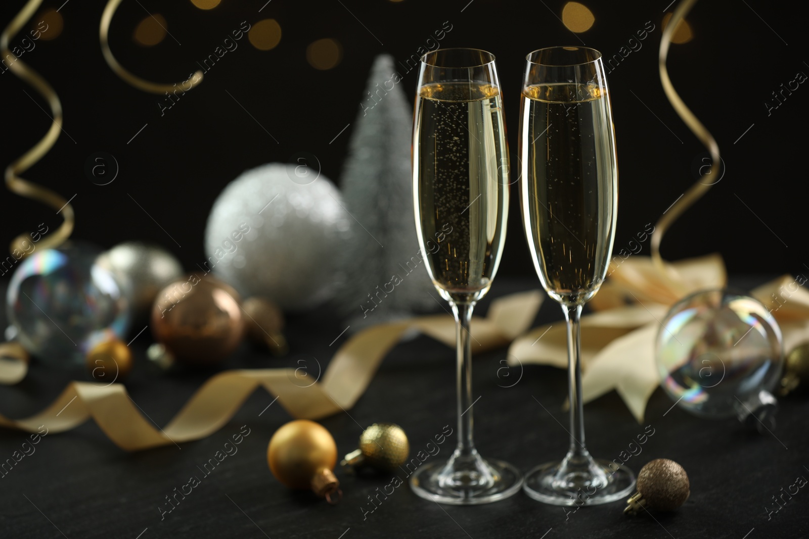 Photo of Delicious champagne in glasses and Christmas decor on black table against blurred lights, space for text