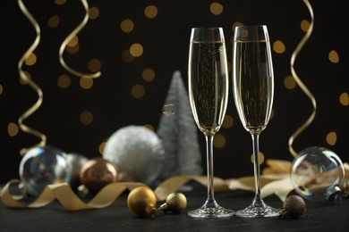 Photo of Delicious champagne in glasses and Christmas decor on black table against blurred lights, space for text