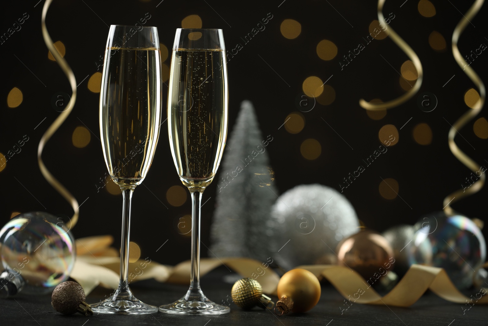 Photo of Delicious champagne in glasses and Christmas decor on black table against blurred lights, space for text