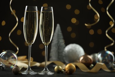 Photo of Delicious champagne in glasses and Christmas decor on black table against blurred lights, space for text