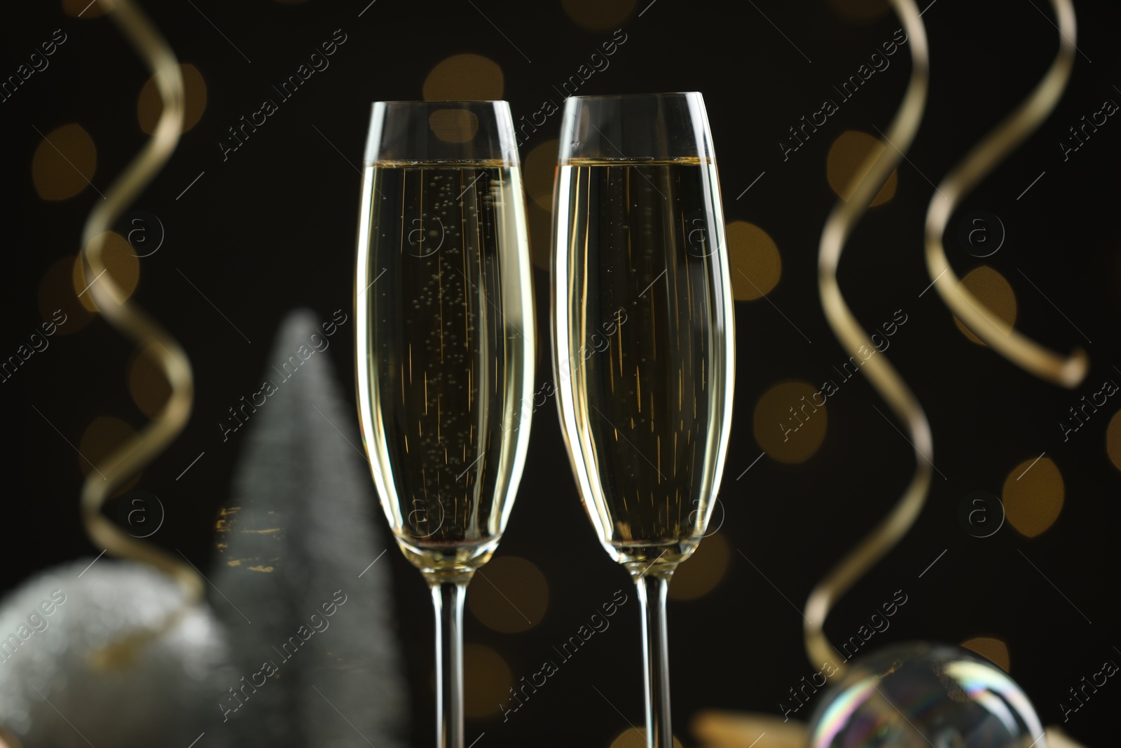 Photo of Delicious champagne in glasses and Christmas decor against black background with blurred lights, closeup