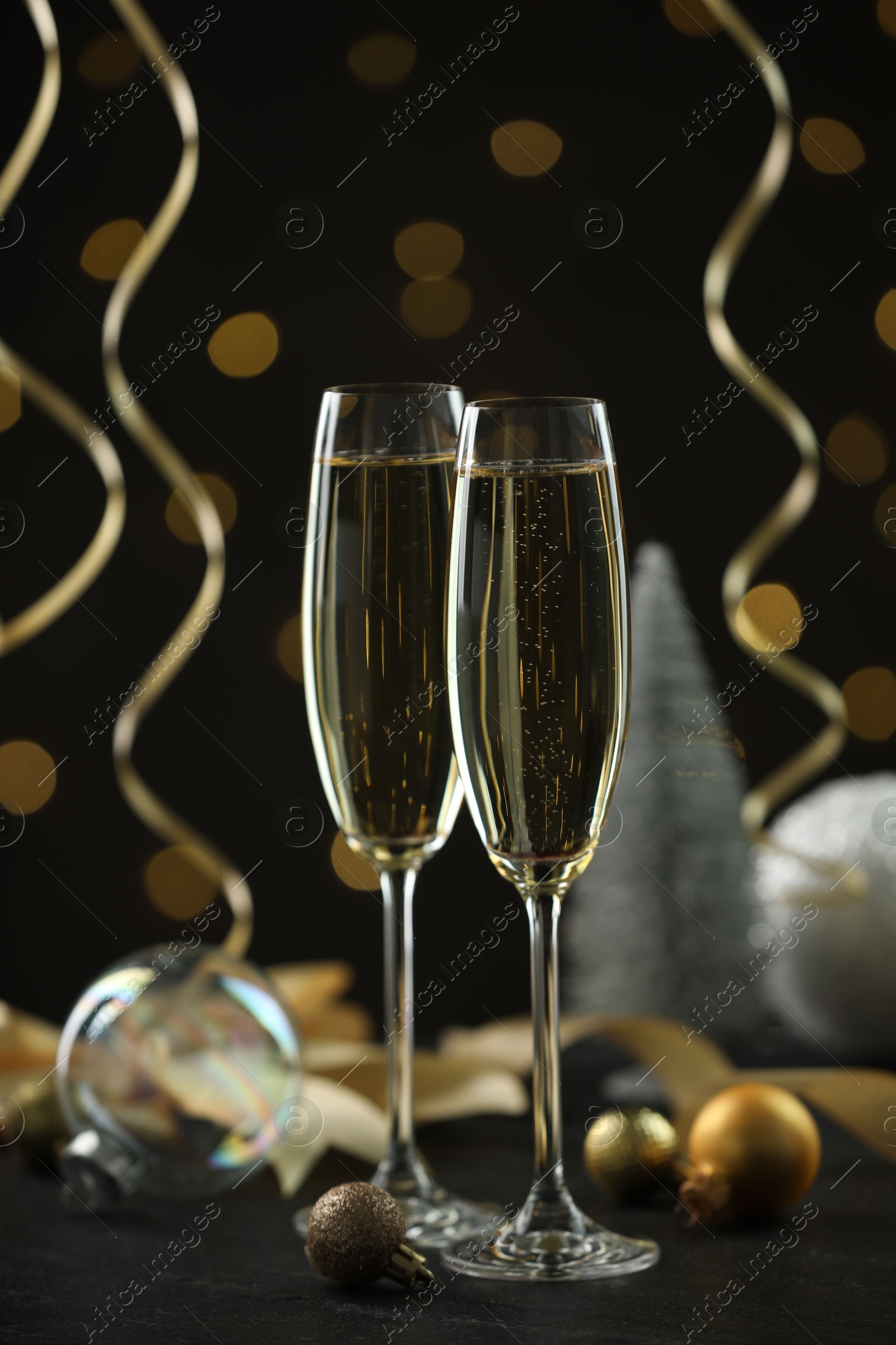 Photo of Delicious champagne in glasses and Christmas decor on black table against blurred lights