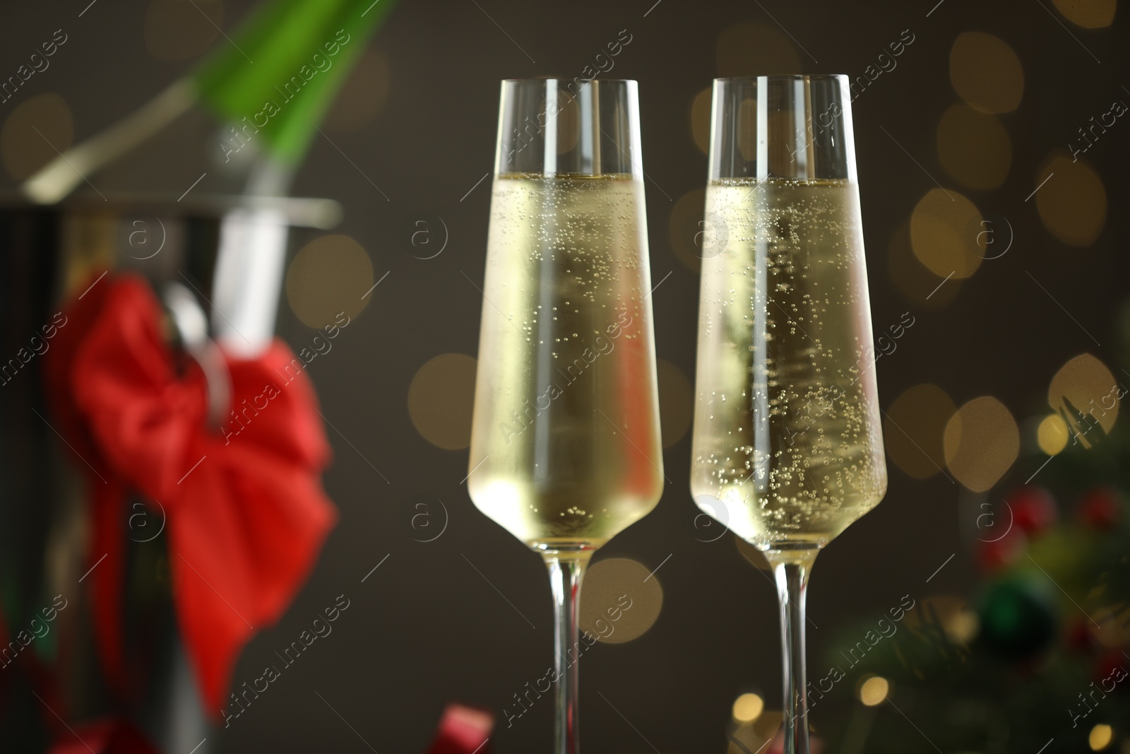 Photo of Delicious champagne in glasses and Christmas decor against grey background with blurred lights, closeup