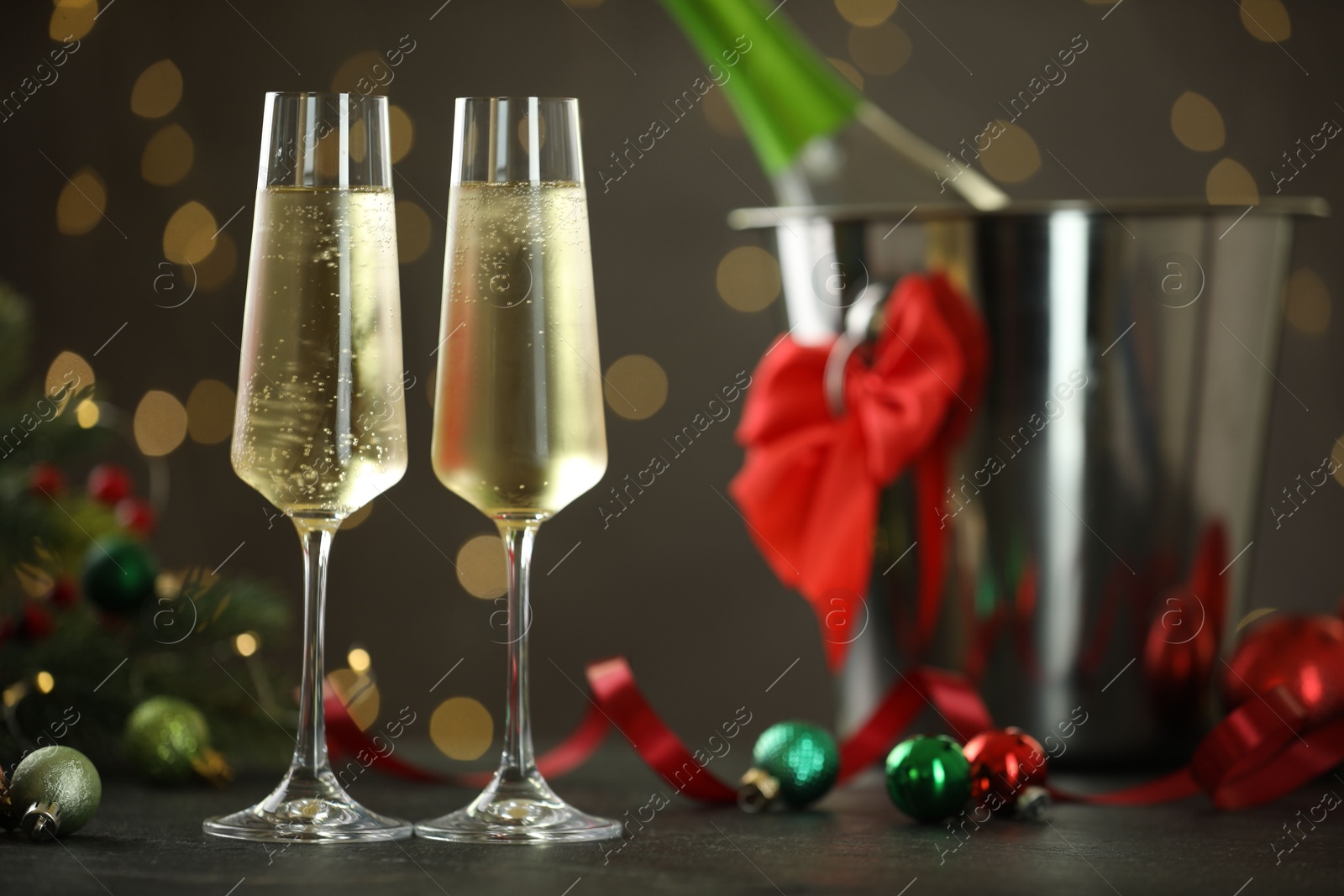 Photo of Delicious champagne in glasses and Christmas decor on grey table against blurred lights, space for text