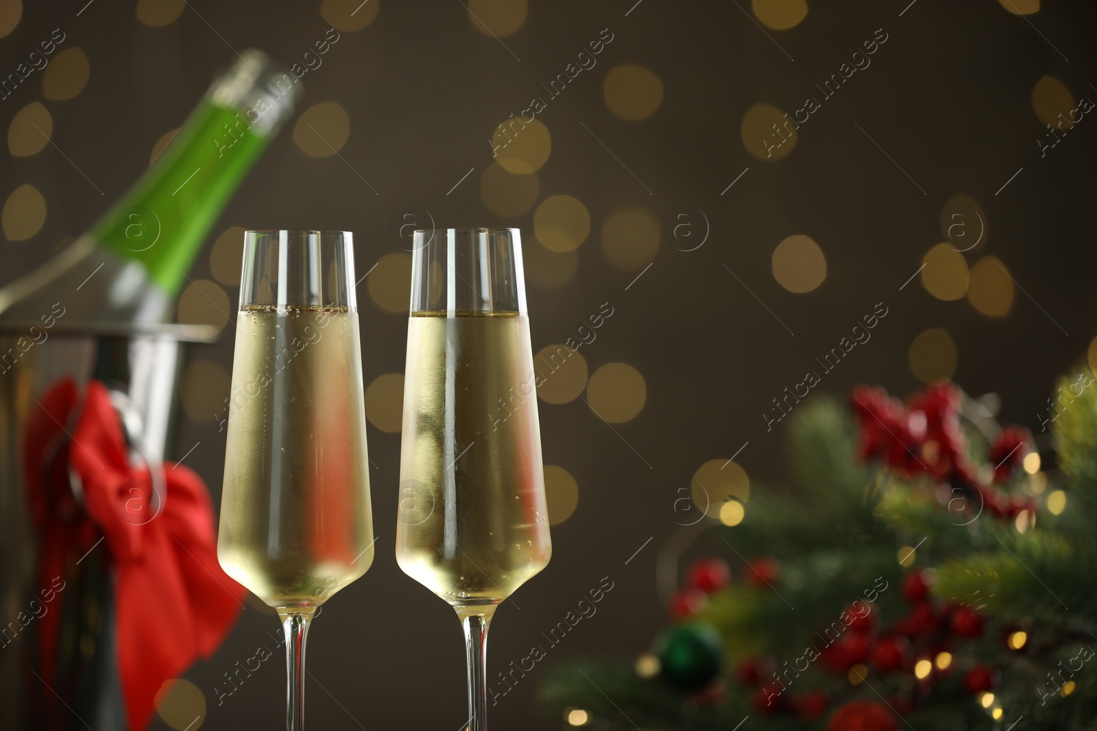 Photo of Delicious champagne in glasses and Christmas decor against grey background with blurred lights, closeup. Space for text