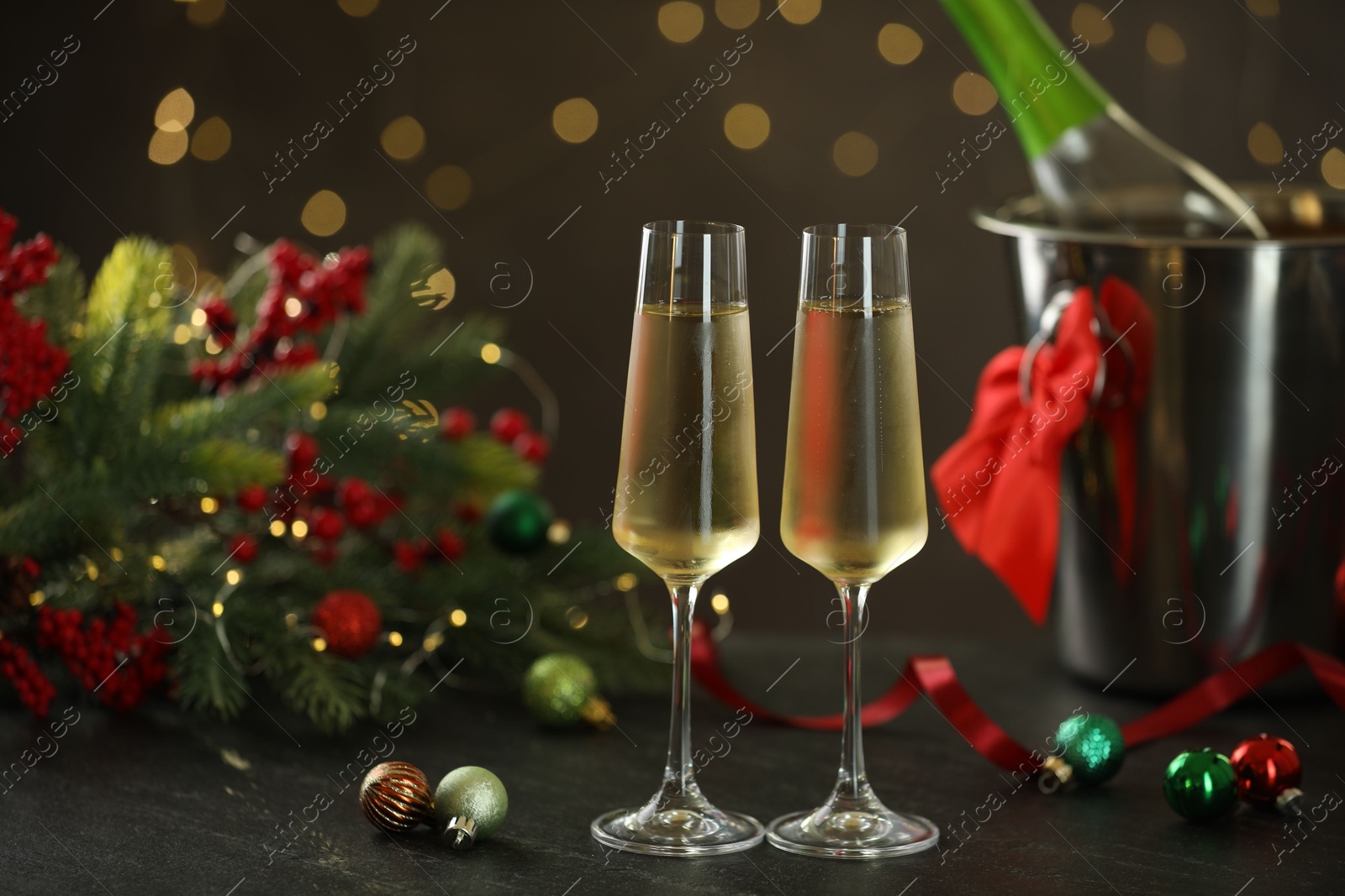 Photo of Delicious champagne in glasses and Christmas decor on grey table against blurred lights, space for text