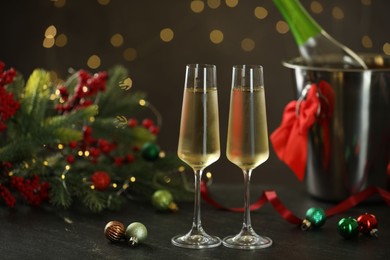 Photo of Delicious champagne in glasses and Christmas decor on grey table against blurred lights, space for text