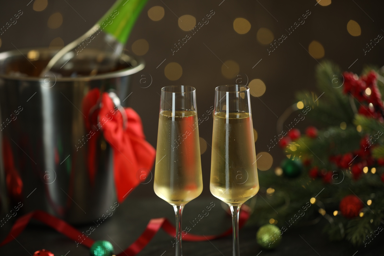 Photo of Delicious champagne in glasses and Christmas decor against grey background with blurred lights, closeup