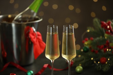 Photo of Delicious champagne in glasses and Christmas decor against grey background with blurred lights, closeup