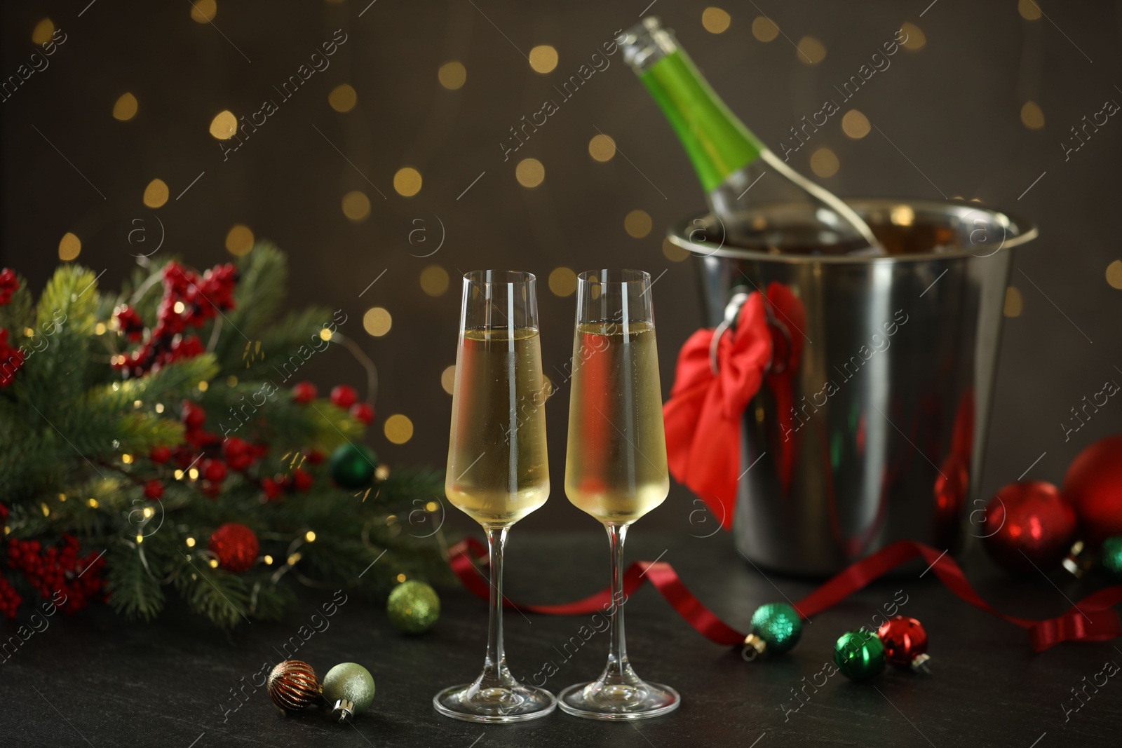 Photo of Delicious champagne in glasses and Christmas decor on grey table against blurred lights